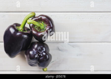 Drei schwarze paprika's auf ein Stück Jute auf eine hölzerne Tafel. Stockfoto