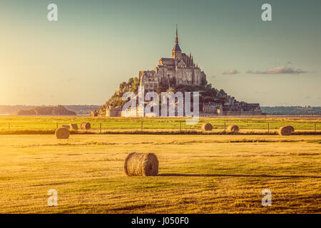 Schöne Aussicht von berühmten historischen Le Mont Saint-Michel im goldenen Abendlicht bei Sonnenuntergang im Sommer mit Heuballen auf Feldern, Normandie, Frankreich Stockfoto