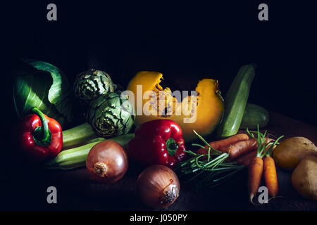 Buntes frisches Gemüse auf schwarzem Hintergrund. Karotten, Kohl, Kürbis, Zwiebeln, Zucchini, Kartoffeln, Tomaten, Artischocken und Paprika. Vintage Sty Stockfoto