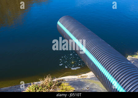 Deponie Sickerwasser Gießen in Teich aus einem schwarzen und blauen Rohr. Ort Ronneby, Schweden. Stockfoto