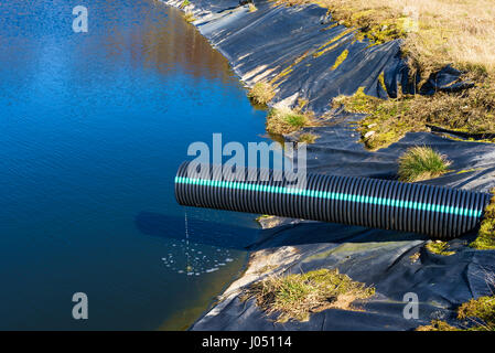 Deponie Sickerwasser Gießen in Teich aus einem schwarzen und blauen Rohr. Ort Ronneby, Schweden. Stockfoto