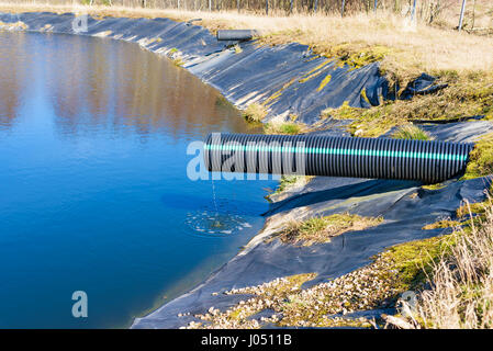 Deponie Sickerwasser Gießen in Teich aus einem schwarzen und blauen Rohr. Ort Ronneby, Schweden. Stockfoto