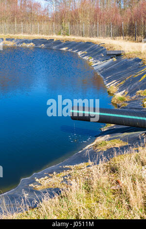 Deponie Sickerwasser Gießen in Teich aus einem schwarzen und blauen Rohr. Ort Ronneby, Schweden. Stockfoto