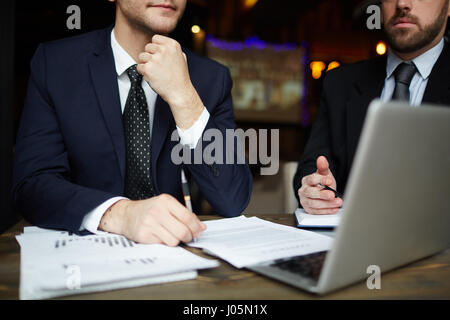 Closeup Portrait zweier unkenntlich erfolgreiche Geschäftspartner tragen schwarze formalen Anzüge Überprüfung Daten mit Laptop am Tisch während der Sitzung Stockfoto