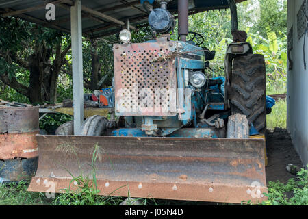 Schmutzige alte Traktor unter einem Schuppen auf dem Hof geparkt Stockfoto