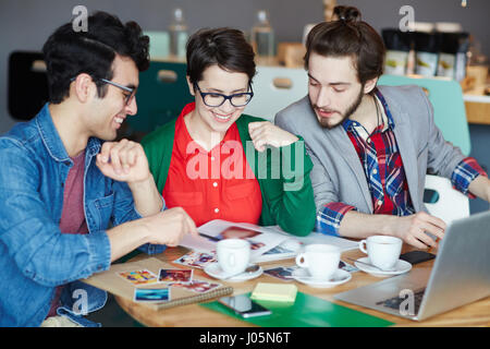 Gruppe von junge kreative Zusammenarbeit bei Treffen im Café und auf der Suche im Magazin mit Fotografien, Lächeln Stockfoto
