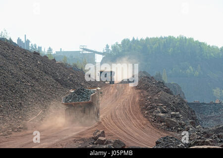 zwei Kipper mit geladenen Steinen in einem Steinbruch entlang fahren. Bergbauindustrie Stockfoto