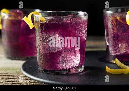 Hausgemachte Purple Haze-Cocktail mit einer Zitrone garnieren Stockfoto