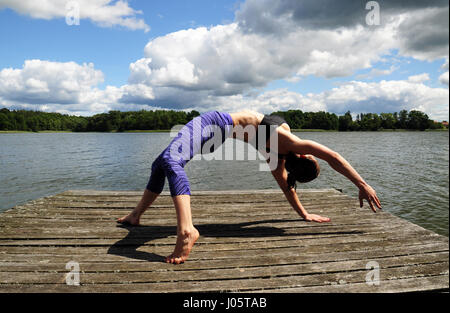 Junge aktive Frau tun Yoga-Positionen auf den Holzsteg am See im polnischen Countsydie in Masuren region Stockfoto