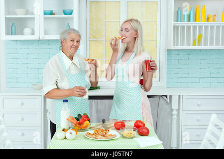 Großmutter und die junge Frau in Küche, schmecken sie die gemachte Pizza. Stockfoto