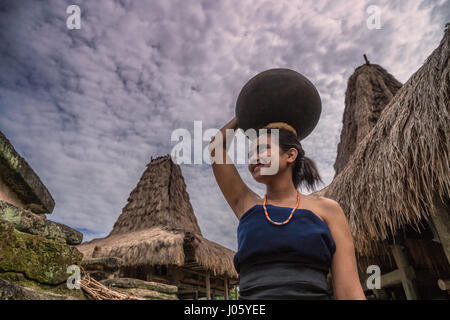 Junge Frau aus dem Loli Stamm trägt einen Wasserkrug auf dem Kopf in ihrem Dorf in West Sumba Stockfoto