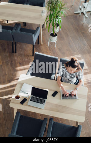Draufsicht der Geschäftsfrau in einem Café am Tisch sitzen und schreiben etwas auf ihrem Laptop. Stockfoto