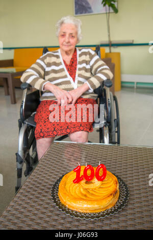 Alte Frau in einem Pflegeheim, auf ihren 100 Geburtstag mit ihrem Geburtstagskuchen. Stockfoto