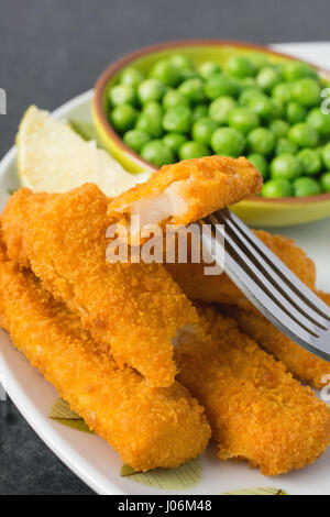 Panierte und gebackene Fischstäbchen, Finger auf einem Teller mit einer Schüssel mit Erbsen und einer Scheibe Zitrone Stockfoto
