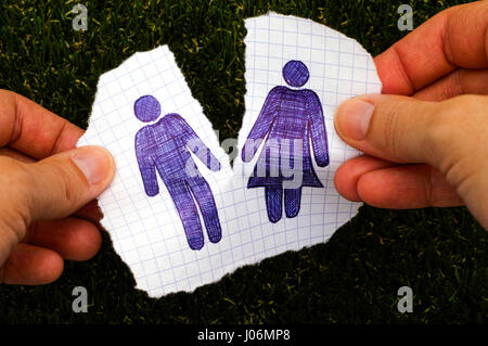 Person Hände Rippen Stück Papier mit handgezeichneten Mann und Frau zahlen. Grass-Hintergrund. Doodle-Stil. Stockfoto