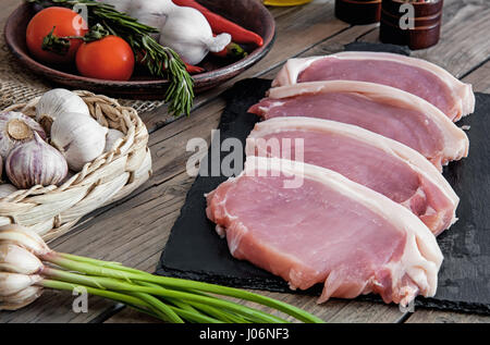 Stücke vom Schwein zum Grillen auf Schiefer Board mit Rosmarin, Knoblauch in einem Weidenkorb, Tomaten im rustikalen Stil Stockfoto