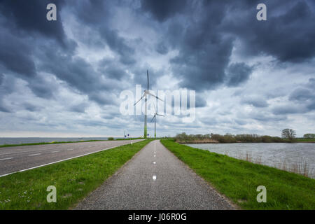 Schöne asphaltierte Straße mit Windkraftanlagen zur Stromerzeugung. Windmühlen zur Stromerzeugung. Landschaft mit Strasse, grünen Rasen und wind m Stockfoto