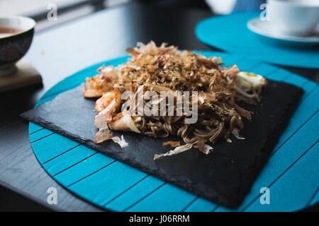Buchweizen-Nudeln mit Garnelen und Späne aus Thunfisch mit Sauce auf schwarze Platte. Asiatische Küche-Hintergrund. Konzept zu essen. Restaurant-Platz mit hölzernen tab Stockfoto