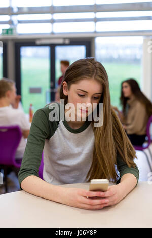 Weibliche Schüler sitzen auf ihrer eigenen Schule. Sie hat eine Smartphone in der Hand die sie anschaut. Stockfoto