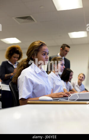 Studenten, die auf Computern in der Schule arbeiten. Die Lehrer können unscharf im Hintergrund gesehen werden. Stockfoto