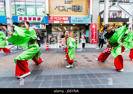 Japan, Kumamoto, Yosakoi Dance Festival. Dance Team in bunten Yukata, 2 Männer auf beiden Seiten, junge jugendmädchen Tänze in Mitte, Auge - Kontakt. Stockfoto