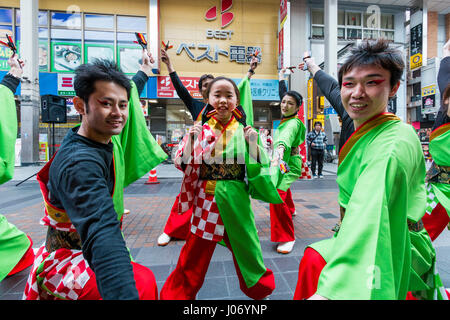 Japan, Kumamoto, Yosakoi Dance Festival. Dance Team in bunten Yukata, 2 Männer auf beiden Seiten, junge jugendmädchen Tänze in Mitte, Auge - Kontakt. Stockfoto