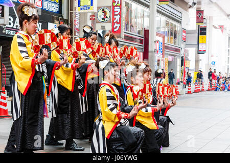 Kumamoto, Japan, Hinokuni Yosakoi Tanzfestival. Teenager Frauenteam, tragen schwarze und gelbe Yukata, kniend und halten Fans, im Einkaufszentrum. Stockfoto