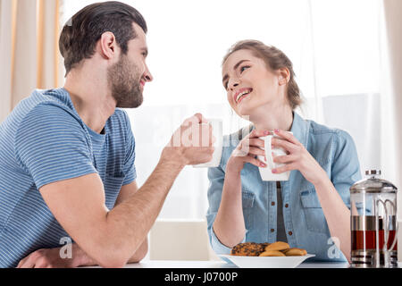 Junges Paar aus weißen Tassen Tee zu trinken und sahen einander lächelnd Stockfoto