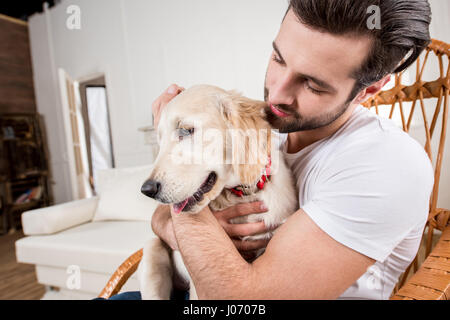 Junger Mann im Schaukelstuhl sitzen und halten süße golden Retriever Welpe Stockfoto