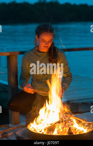 Teenager-Mädchen stand in der Nähe Lagerfeuer am Dock, Lake Of The Woods, Ontario, Kanada Stockfoto