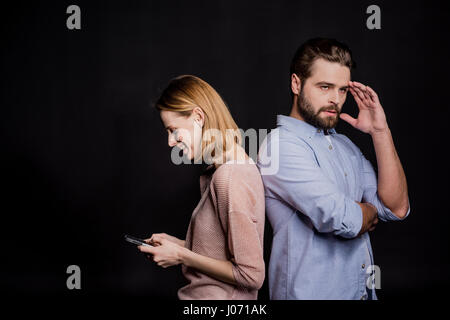 Junge Frau mit Smartphone stehen Rücken an Rücken mit nachdenklicher Mann Stockfoto