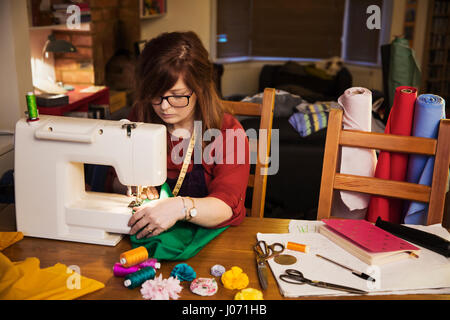 Eine Frau mit einer elektrischen Nähmaschine auf einem Tisch, umgeben von Papieren und Nähen und Handwerk Ausrüstung und Schrauben des Tuches. Stockfoto