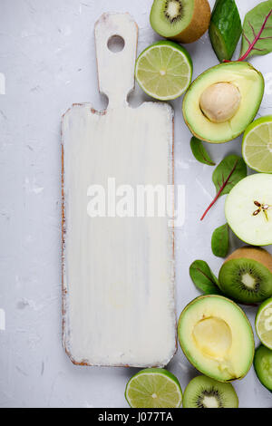 Rahmen der grüne Gemüse und Früchte weiß Holzbrett über leichte graue Putz Tisch, Essen Hintergrund mit freiem Speicherplatz für text Stockfoto