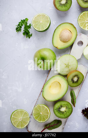 Rahmen der grüne Gemüse und Früchte weiß Holzbrett über leichte graue Putz Tisch, Essen Hintergrund mit freiem Speicherplatz für text Stockfoto