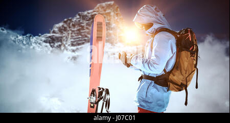 Skifahrer mit Ski und Rucksack mit Handy gegen Blick auf verschneite Gebirge und Wolken Stockfoto