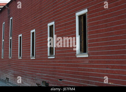 Eine Reihe von leeren Fenster Buchten erstrecken sich auf der Seite der verwitterten rot lackierten Schindeln Wand. Stockfoto