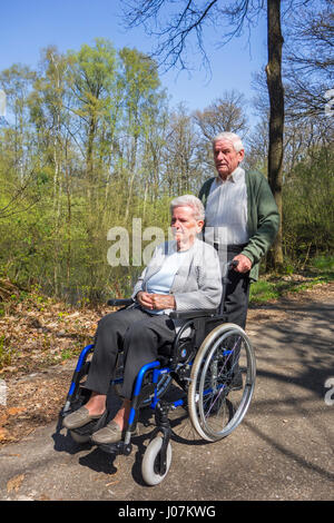 Pensionierter Mann unter deaktiviert ältere Frau im Rollstuhl für einen Spaziergang im Park an einem sonnigen Tag im Frühling Stockfoto