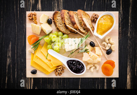 Käseplatte mit Scheiben Brot, Trauben, getrocknete Aprikosen, Oliven, Marmelade, Honig und Nüssen auf hölzernen Hintergrund serviert Stockfoto