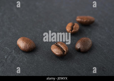 Einige geröstete Kaffeebohnen Makro erschossen auf einem schwarzen Stein Schiefer Teller Stockfoto