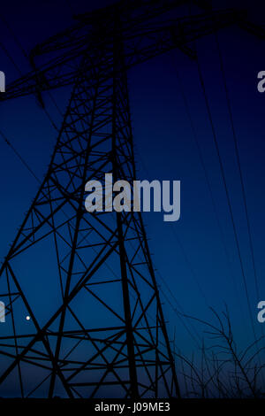 große elektrische Energie Turm bei Sonnenuntergang mit einem gelben Mond im Hintergrund Stockfoto