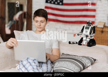 Es ist einfach. Attraktive junge sitzt auf dem Sofa, Blick auf den Bildschirm des Computers, indem sein Spielzeug in der Nähe von ihm Stockfoto