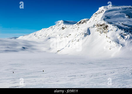 Schneebedeckte Berge, blauer Himmel, Das arktische Norwegen mit 2 Skitourengeher im Vordergrund Stockfoto