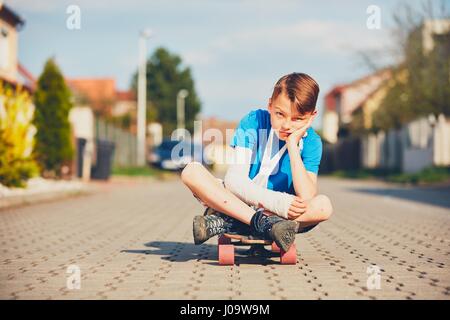 Schelmische Junge mit gebrochenen Hand verletzt nach Unfall auf Skateboard. Stockfoto