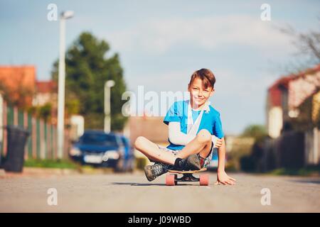 Schelmische Junge mit gebrochenen Hand verletzt nach Unfall auf Skateboard. Stockfoto