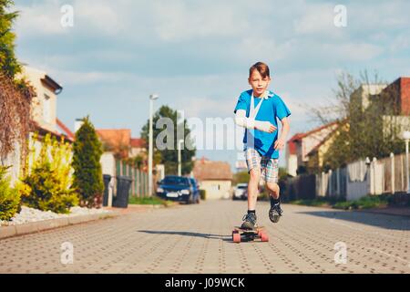 Schelmische Junge mit gebrochenen Hand verletzt nach Unfall auf Skateboard. Stockfoto