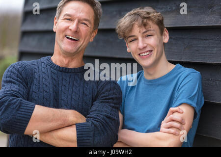 Porträtaufnahme eines attraktiven, erfolgreichen und glücklichen Mitte im Alter Mann Vater männliche mit seinem jungen Sohn vor Lachen Teen, verschränkten Arms tragen ein Stockfoto