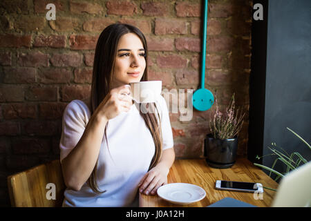 Porträt des jungen wunderschöne weibliche Tee trinken und mit Lächeln aus dem Coffee-Shop-Fenster und genießen Sie ihre Freizeit Stockfoto