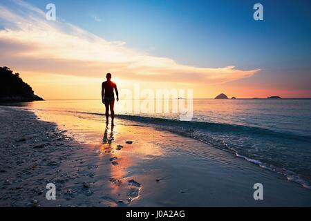 Einsamer Mann während traumhaften Sonnenuntergang am tropischen Strand zu Fuß. Perhentian Inseln, Malaysia Stockfoto