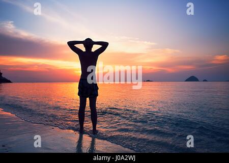 Nachdenklicher junger Mann im Wasser auf das tropische Meer bei Sonnenuntergang steht. Stockfoto