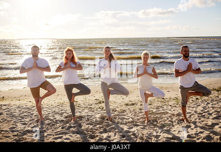 Gruppe von Menschen, die Yoga in Baumpose am Strand Stockfoto